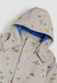 Beige Regenjacke mit blauer Innenausstattung, geschmückt mit bunten Dinosaurier- und Palmenmustern. Enthält eine Kapuze und einen Klettverschluss.