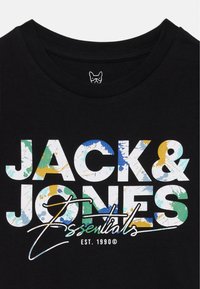 Black t-shirt featuring bold, colorful text reading "JACK & JONES Essentials" with a signature-style logo above. Established 1990.