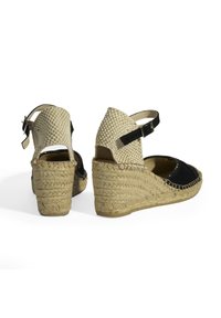 Sandales compensées en suède noir avec une bride de cheville tissée beige et un talon en jute. Présentent un design à bout ouvert et une fermeture à boucle.