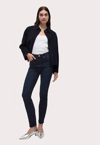 Chaqueta azul marino con botones, camiseta de tirantes blanca, jeans ajustados oscuros y zapatos de tacón plateados. Diseño sencillo con líneas elegantes y texturas suaves.