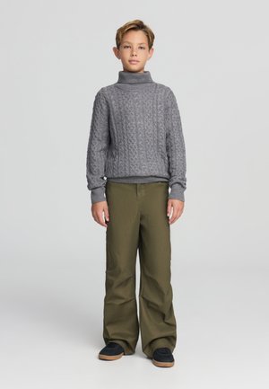 Maglione grigio a maglia grossa con colletto alto e polsini a costine abbinato a pantaloni larghi verdi oliva e sneaker nere con suola beige.