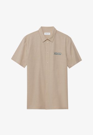 Camicia beige a maniche corte realizzata in un tessuto leggero, con colletto e chiusura frontale a bottoni. Include un testo ricamato in blu sul petto.