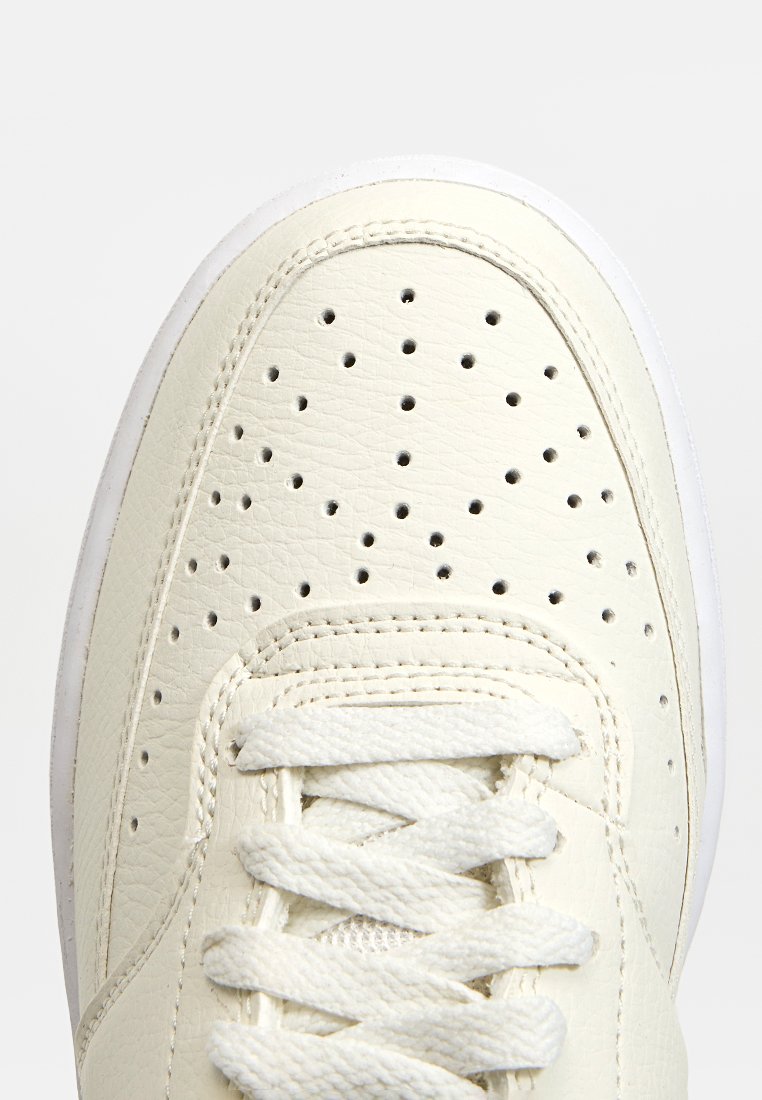 Weiße Leder-Sneaker mit perforiertem Zehenbereich, flachen weißen Schnürsenkeln, gepolsterter Schuhmanschette und weißer Gummisohle. Strukturiert Oberfläche mit sichtbaren Nähten.