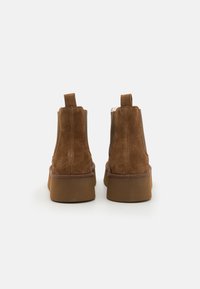 Brune semskede ankelstøvler med rund tå, elastiske sidepaneler og en tyk gummisål. Har en pull-tab for nem påtagning.