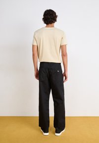 T-shirt en coton beige et pantalons cargo noirs avec poches latérales. Coupe décontractée, encolure ronde standard et logo dans le dos. Baskets blanches.