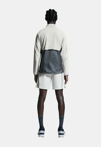 Veste légère bicolore avec une partie inférieure grise et une partie supérieure beige. Elle possède des manches longues et un col montant. Associée à un short blanc.