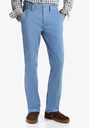 Hellblaue Baumwollhosen mit glatter Textur, geradem Schnitt und Seitentaschen, kombiniert mit braunen Sneakers.