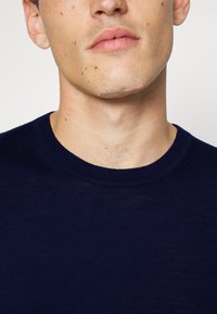 Marineblå strikkegenser med rund hals, med ribbestrikket krage og subtil tekstur. Glatt stoff og minimale designdetaljer.