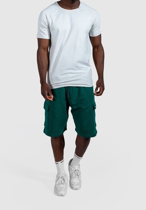 Chemise gris clair à manches courtes raglan, associée à un short cargo turquoise avec poches latérales. Port de baskets blanches et de chaussettes.