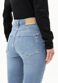 Hoge taille blauwe jeans van lichtgewassen denim, met een leren label met "ARMEDANGELS." Vier zakken en een getailleerd ontwerp.