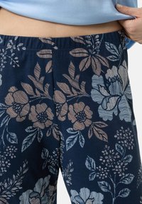 Kukkakuosiset yöpaita housut tummansinisenä, joissa on vaaleanruskeita ja sinisiä abstrakteja kukkakuoseja. Elastinen vyötärö, pehmeä kangas ja väljä istuvuus.