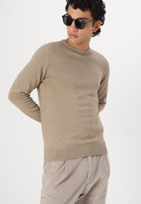 Μπεζ πουλόβερ με στρογγυλή λαιμόκοψη και ραμμένα μανίκια, συνδυασμένο με ανοιχτό γκρι καμβά παντελόνι. Διαθέτει λεία υφή και εφαρμοστή σχεδίαση.