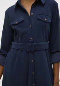 Robe boutonnée bleu marine en tissu côtelé, dotée de deux poches poitrine, d'une taille ceinturée et de manches retroussées avec des boutons dorés.