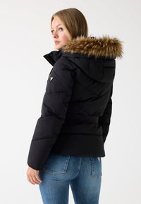 Zwarte pufferjack met een faux fur-voering in de capuchon, een ceintuur in de taille en een diagonale gestikte ontwerp. Gecombineerd met blauwe denimjeans.