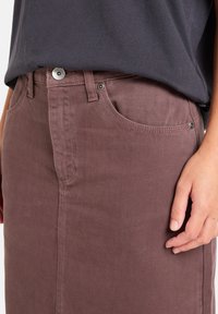 Vaaleanruskea corduroy-hame, jossa on etupockets, hopeinen nappisuljenta ja suora siluetti. Hameen pinnassa on teksturoitua kangasta ja hienovaraista ompelua.