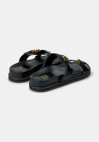 Sandali platform neri con cinghie incrociate, dettagli con fibbie in tonalità oro e una superficie liscia. La suola presenta una leggera curvatura e il marchio.