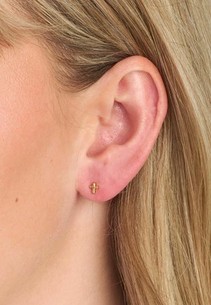 Cercei cu tija în formă de cruce din aur, cu o suprafață texturată, având un design minimalist. Purtați pe urechea stângă, pe piele netedă.