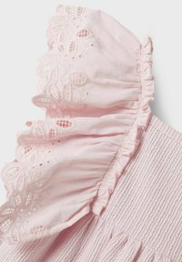 Rosa bomullstopp med volangkrage och broderade spetsdetaljer samt smockad textur på bodice. Mjuk och lättviktsmaterial.