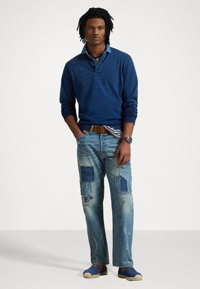 Blå långärmad polo med en kontrasterande ljusblå krage, parat med slitna ljusa denimjeans med lappar och blå skor.