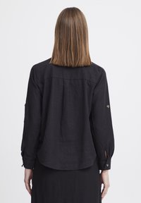 Maglietta nera a maniche lunghe con una vestibilità rilassata, realizzata in lino. Presenta dettagli con bottoni sulle maniche e un orlo leggermente curvo. Design semplice.