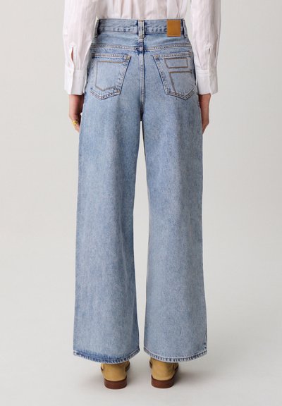 Jeans in denim blu chiaro a gamba larga con vita alta, due tasche sul retro e una toppa in pelle marrone con il marchio sulla cintura.