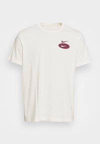 T-shirt z krótkim rękawem, okrągłym dekoltem w kolorze off-white wykonany z bawełny z bordowym logo Nike na lewej piersi, o gładkiej fakturze i standardowym kroju.