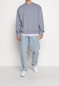 Sweat-shirt gris clair à col rond avec logo brodé. Associé à un jean bleu clair ample et des baskets blanches. Coupe décontractée et texture douce.