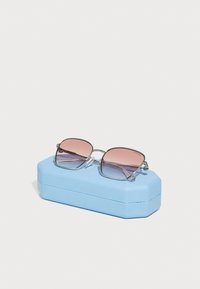 Ochelari de soare pătrați cu ramă argintie și lentile roz cu nuanțe gradient, așezați pe o carcasă texturată de bleu deschis.