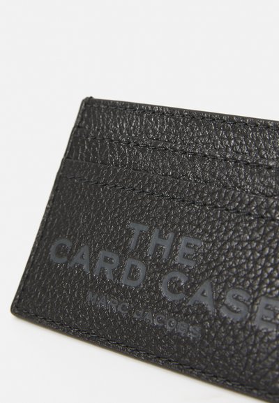 Svart strukturerad läderkortfodral med flera kortfack och präglad text "THE CARD CASE MARC JACOBS" på framsidan.
