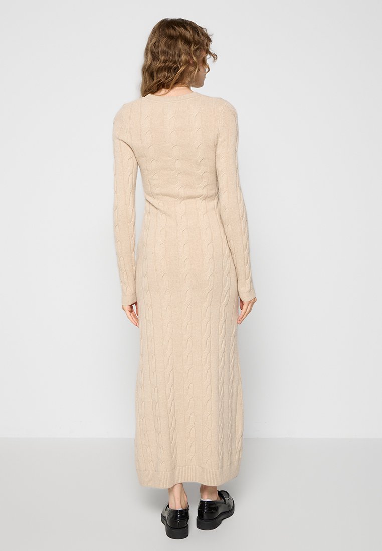 Beige gestricktes langes Kleid mit Zopfmuster, langen Ärmeln und taillierter Silhouette, das knapp über den Knöcheln endet. Glatte Textur.