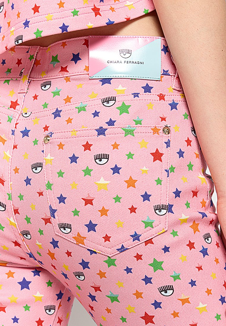 Jeans en denim rose avec un motif d'étoiles multicolores et des motifs d'yeux. Comprend une étiquette de marque à l'arrière et des détails de couture visibles.