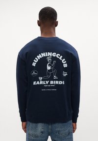 Granatowy sweatshirt wykonany z bawełny, z graficznym nadrukiem na plecach przedstawiającym postać oraz tekstem promującym klub biegowy.