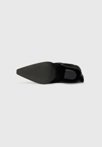 Bottine noire à talon avec un bout pointu, une tige texturée et une semelle en caoutchouc lisse. Présente des coutures blanches contrastantes le long de la couture.