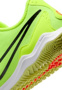 Zapatilla deportiva de neón verde brillante con una parte superior de tela texturizada, líneas negras de acento, entresuela blanca y suela de goma con un patrón en amarillo y rojo.