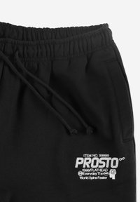 Czarne dresy mają elastyczny pas ze sznurkiem, miękką fakturę, boczne kieszenie oraz srebrne hafty z logo i detalami "PROSTO".