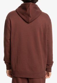 Bordeaux hoodie gemaakt van zachte stof, met een ontspannen pasvorm, geribbelde manchetten en een kangoeroezak. Soepele textuur met een eenvoudig ontwerp.