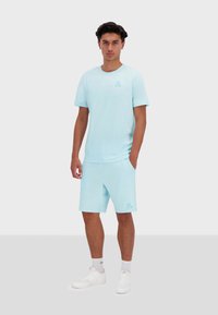 Světle modré tričko s krátk�ým rukávem a odpovídající šortky, bavlněný materiál, volný střih, minimální branding na hrudi a šortkách. Bílé tenisky.