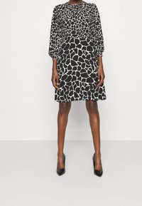 Svart och vit klänning med giraffmönster, långa puffärmar, figurnära liv och utsvängd kjol. Matchad med svarta högklackade skor.