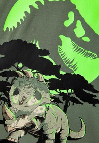 Koszulka graficzna z dinozaurem, z zielono-czarnym wzorem. Ilustracja przedstawia triceratopsa na tle oświetlonym przez księżyc.