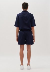 Marineblauw shirt met korte mouwen en bijpassende shorts van lichtgewicht stof, voorzien van een relaxte pasvorm en een rugzakdetail. Witte sneakers inbegrepen.