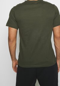Camiseta de algodón verde oliva con mangas cortas, escote redondo y un diseño ajustado. Sin logotipos ni patrones visibles en la parte posterior.
