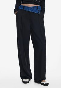 Schwarze weit geschnittene Hosen mit einem blauen Denim-Gürtel, mit Falten, einer glatten Textur und einem lässigen Schnitt. Akzente umfassen ein Knopfdetail.