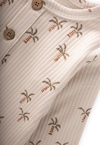 Ribbad tygtopp i beige med palmer och morotsmotiv i brunt och rost. Dekorerad med knappar i trä vid halsringningen.