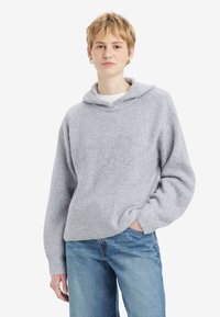 Light gray knitted pullover with a hood, wide sleeves, and a ribbed texture. Paired with loose blue jeans.