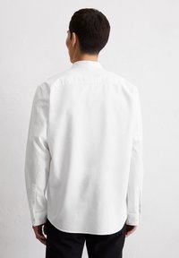 Witte lange mouwen shirt met een puntige kraag, knopenmanchetten en een gebogen zoom. De stof lijkt glad en lichtgewicht.