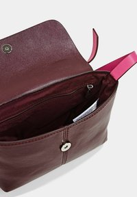 Burgundin värinen nahkalaukku, jossa on sileä pinta, vaaleanpunaiset hihnat, magneettikiinnitys ja sisäinen vetoketjullinen tasku. Auki oleva näkymä, joka esittelee lokeroita.