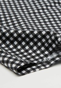 Czarna i biała kratka z małymi kwadratami, charakteryzująca się miękką teksturą i widocznym szwem wzdłuż krawędzi.