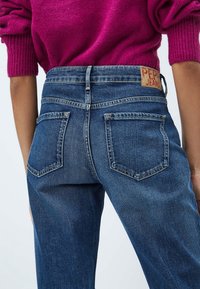 Tummansiniset farkut, joissa on kaksi takataskua, korkea vyötärö ja ommeltu etiketti vyötärönauhan kohdalla. Sileä pinta ja klassinen leikkaus.