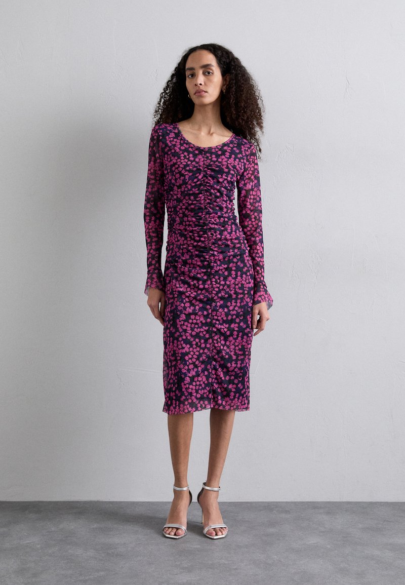 Robe cintrée à manches longues avec un motif floral noir et rose, détails de fronces texturées et ourlet au niveau des genoux. Talons ouverts argentés.