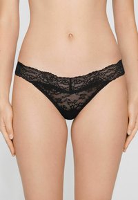 Schwarzer Spitzen-String mit floralem Muster, ausgestattet mit einem breiteren Spitzenbund und zartem Mesh-Gewebe, das durchsichtige Abdeckung und filigrane Details bietet.